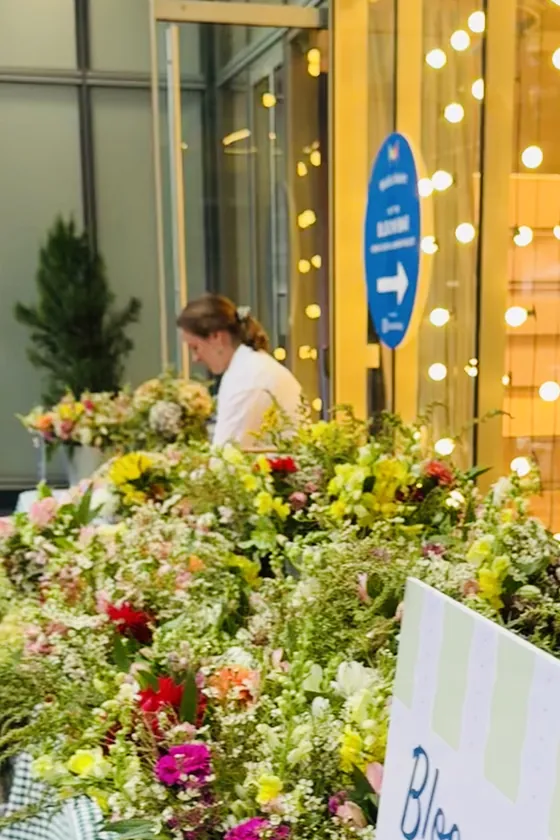 Alba behind buckets of flowers at the bloom bar, string lights in the window behind